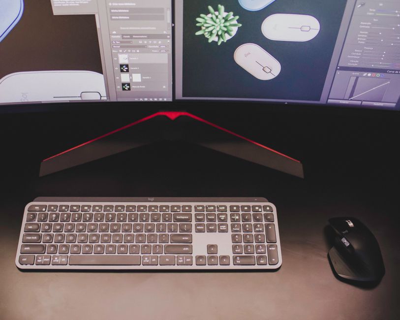 Close-up of a stylish workspace featuring a keyboard and mouse with dual monitors displaying design software.